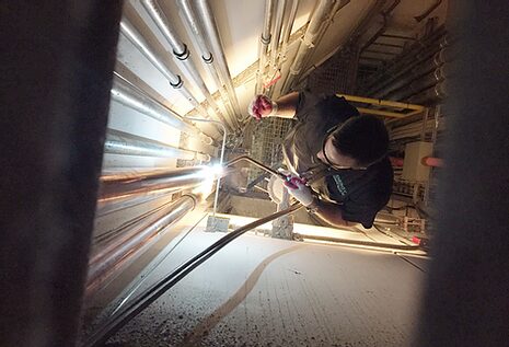 Technician welding copper pipes inside utility shaft